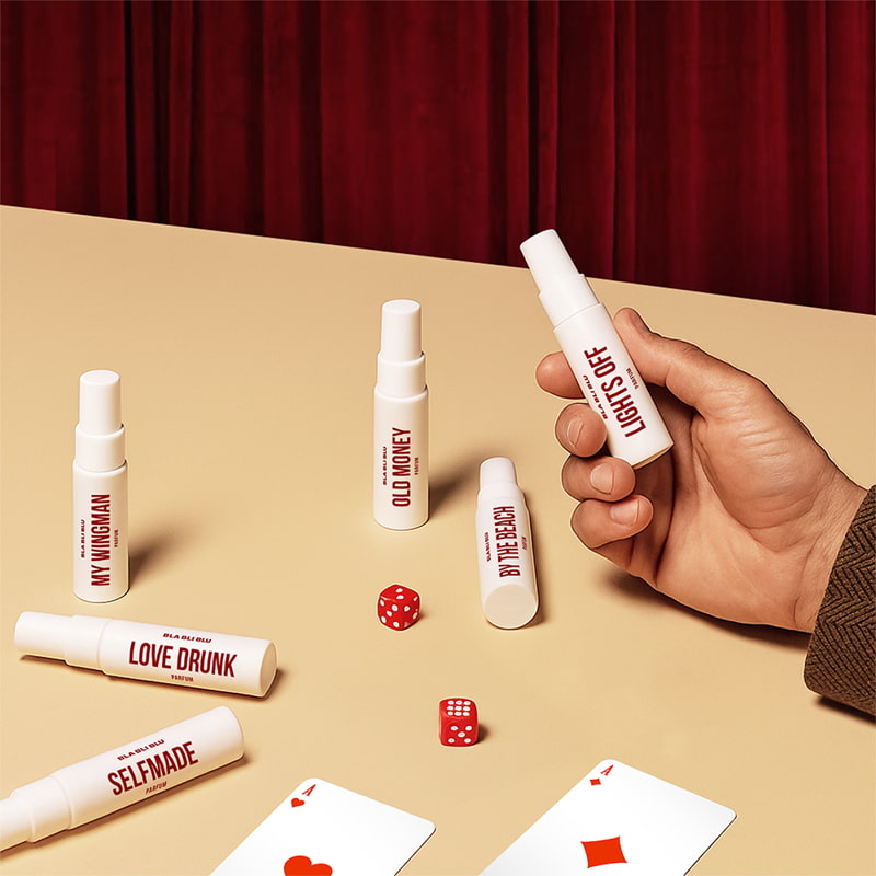 Hand holding a small spray bottle labeled 'LIGHTS OFF' on a beige surface with other similar bottles and playing cards.