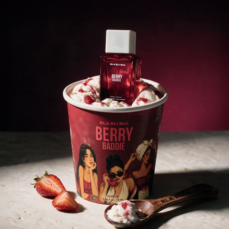 A red Bla bli blu 'Berry Baddie' fragrance bottle is displayed inside a matching red berry flavored cup filled with whipped cream.