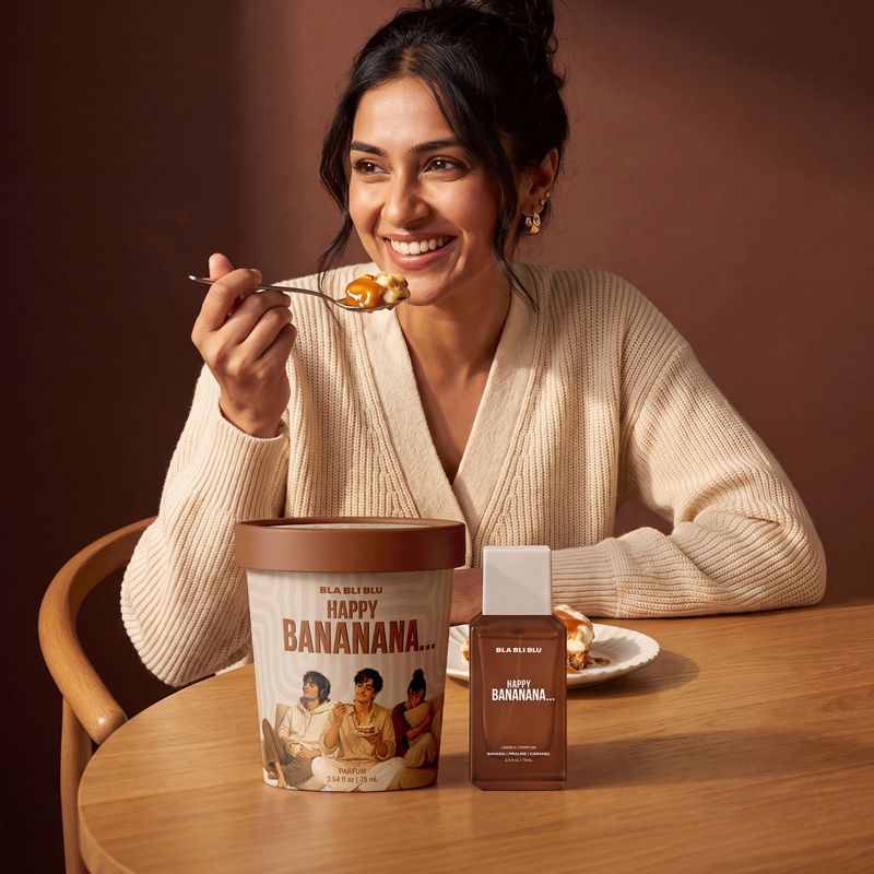 A woman smiling at a wooden table, holding a spoon with banana perfume.
