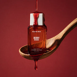 A bottle of BLA BLi blu BERRY BADDIE strawberry jam cream is held on a wooden spoon with glossy.