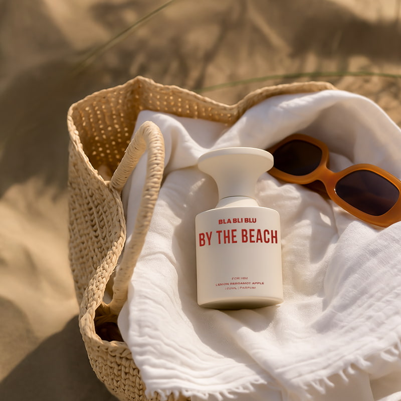 Men Perfume bottle labeled 'By the Beach' and sunglasses on a textured surface
