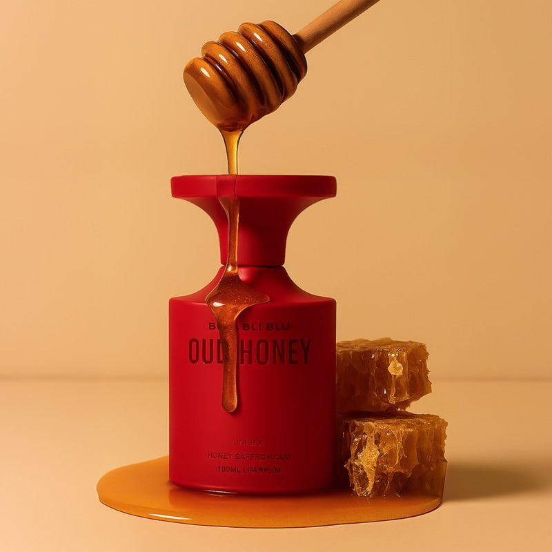 Red bottle labeled 'Oud Honey' with honey being dripped from a wooden dipper onto a beige background.