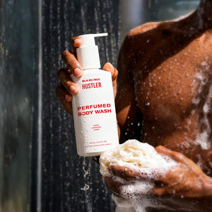 Person holding a bottle of Hustler Perfumed Body Wash under a shower.